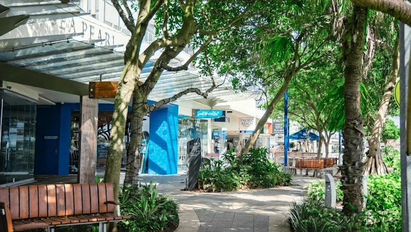 Mooloolaba Esplanade shopping precinct with shaded walkway, tropical trees and Pacific Beach signage